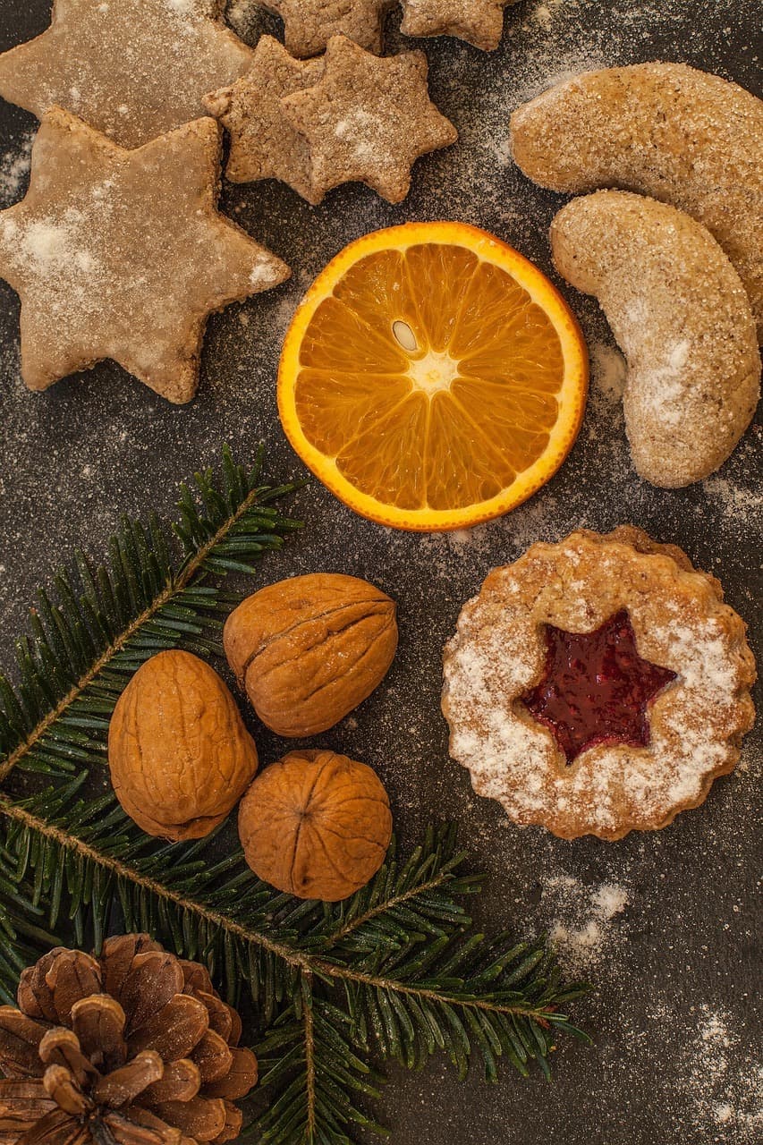 Weihnachtsplätzchen von oben: Sternplätzchen, Vanillekipferl und ein Spitzbube, dazu eine Orangenscheibe, Walnüsse und Tannenzweige